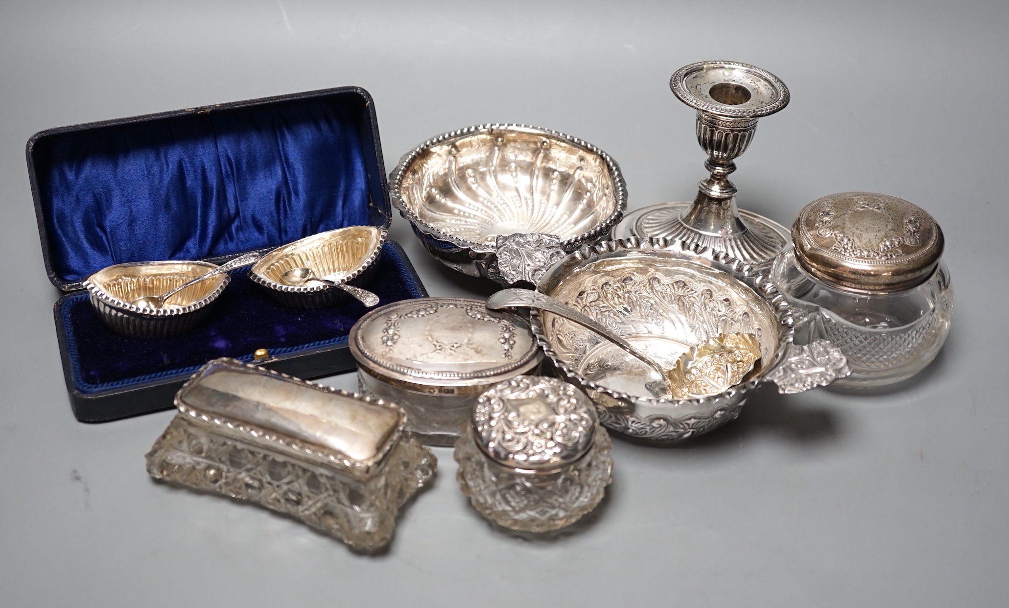 A Victorian repousse silver two handed bowl, one other silver bowl, a silver sifter spoon, four silver mounted glass toilet jars, a silver dwarf candlestick and a cased pair of silver salts.